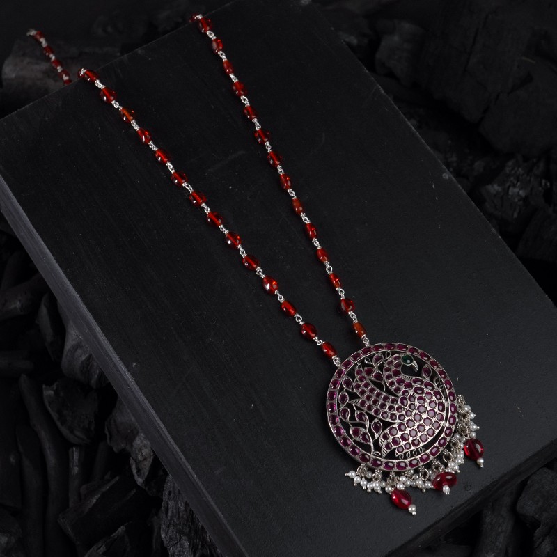 long silver necklace with red oval beads and a kemp stone filled peacock pendant