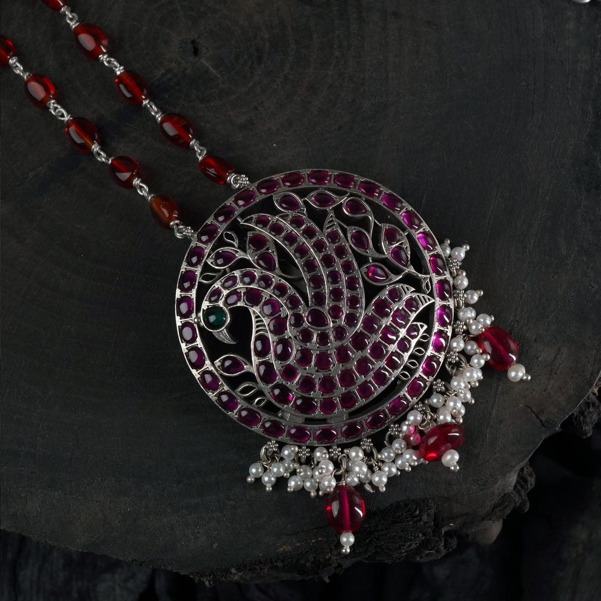 long silver necklace with red oval beads and a kemp stone filled peacock pendant