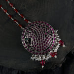 long silver necklace with red oval beads and a kemp stone filled peacock pendant