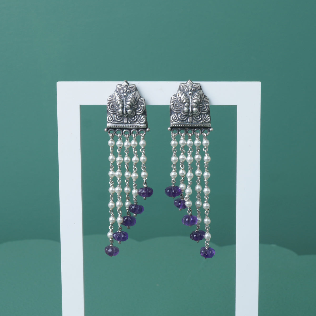 a photo of silver earrings studded with pearls and amethyst beads on a stand