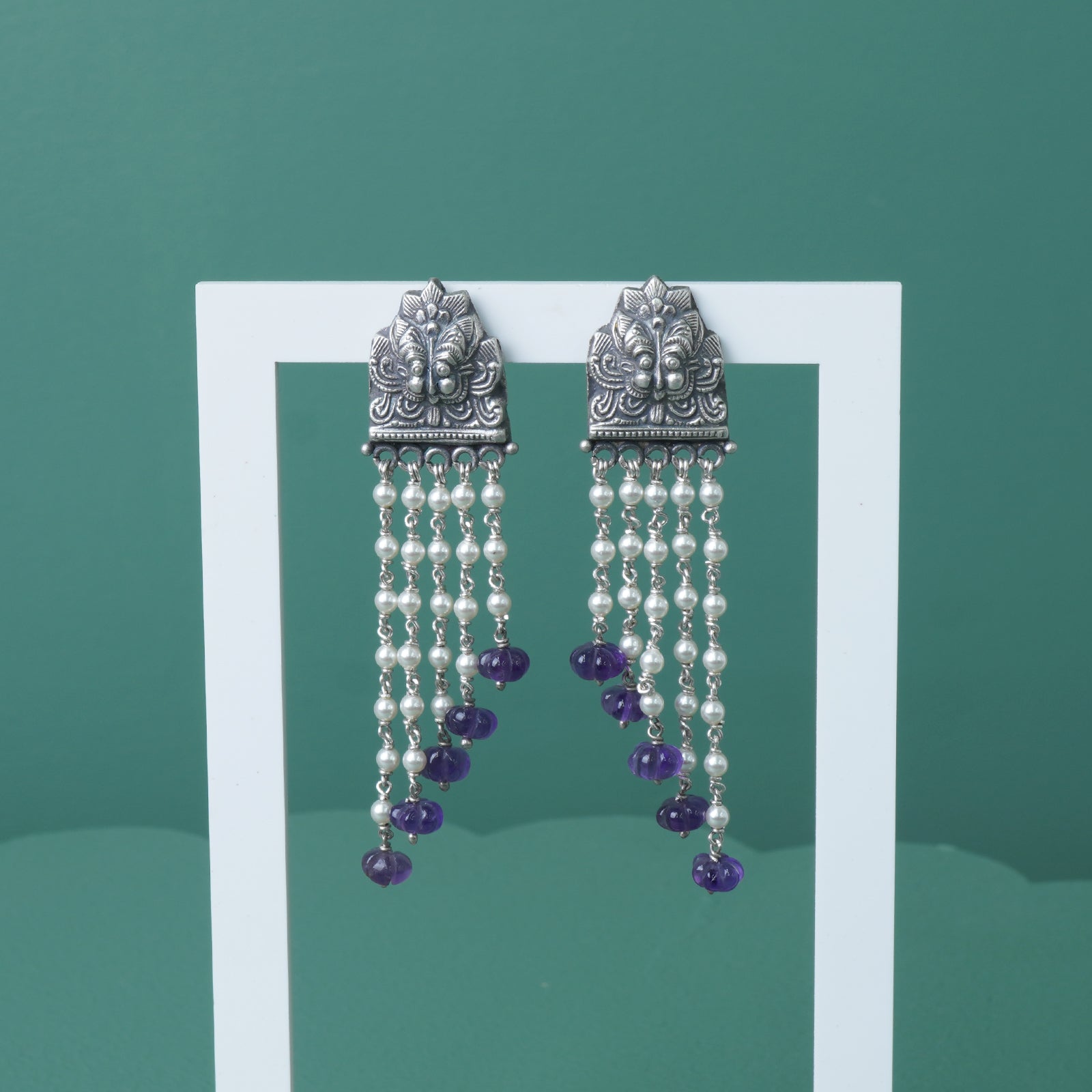 a photo of silver earrings studded with pearls and amethyst beads on a stand