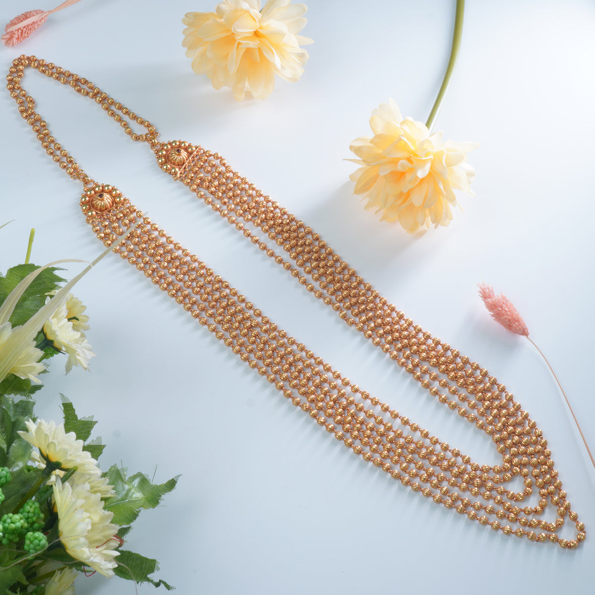 Gold beaded necklace on a light blue background with flowers