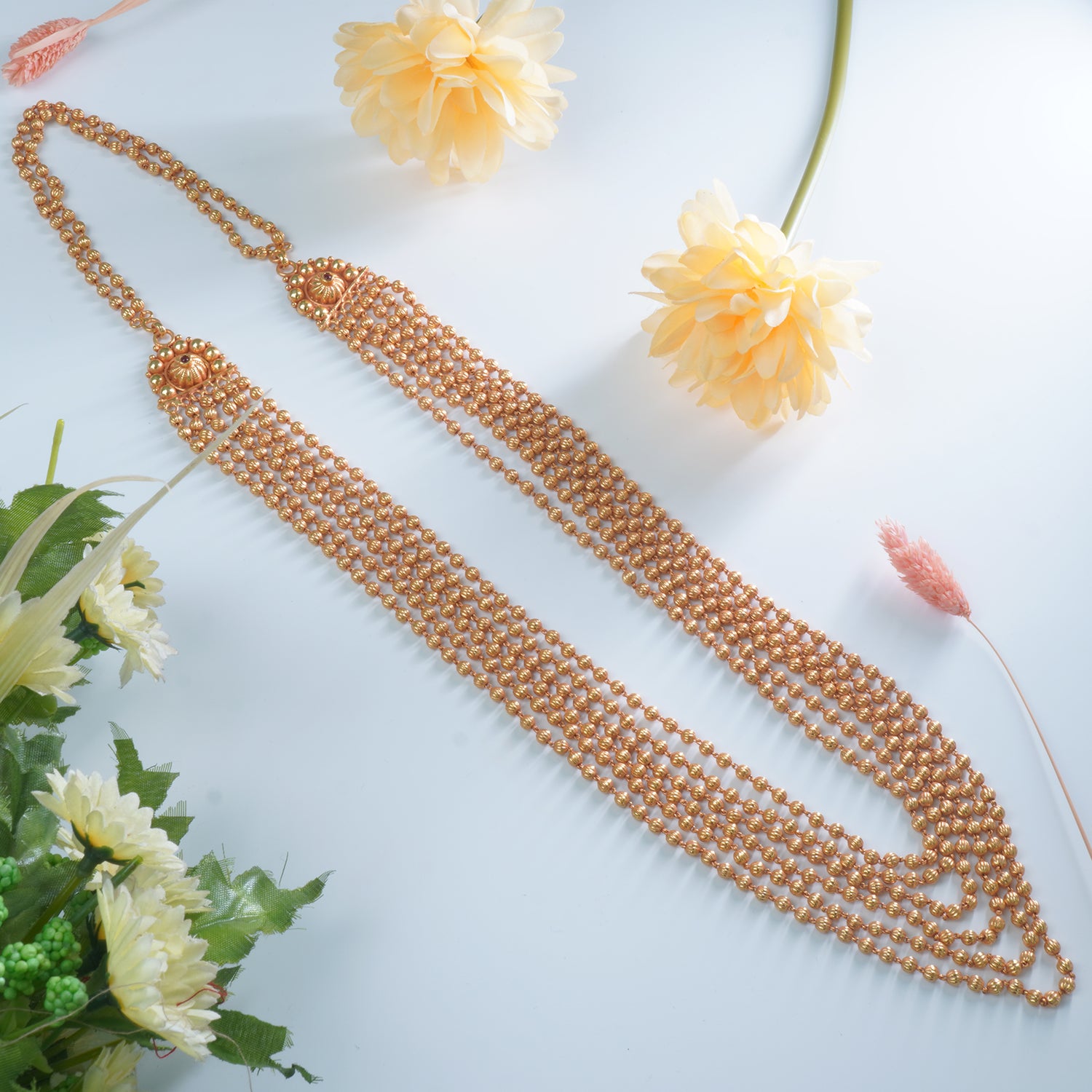 Gold beaded necklace on a light blue background with flowers