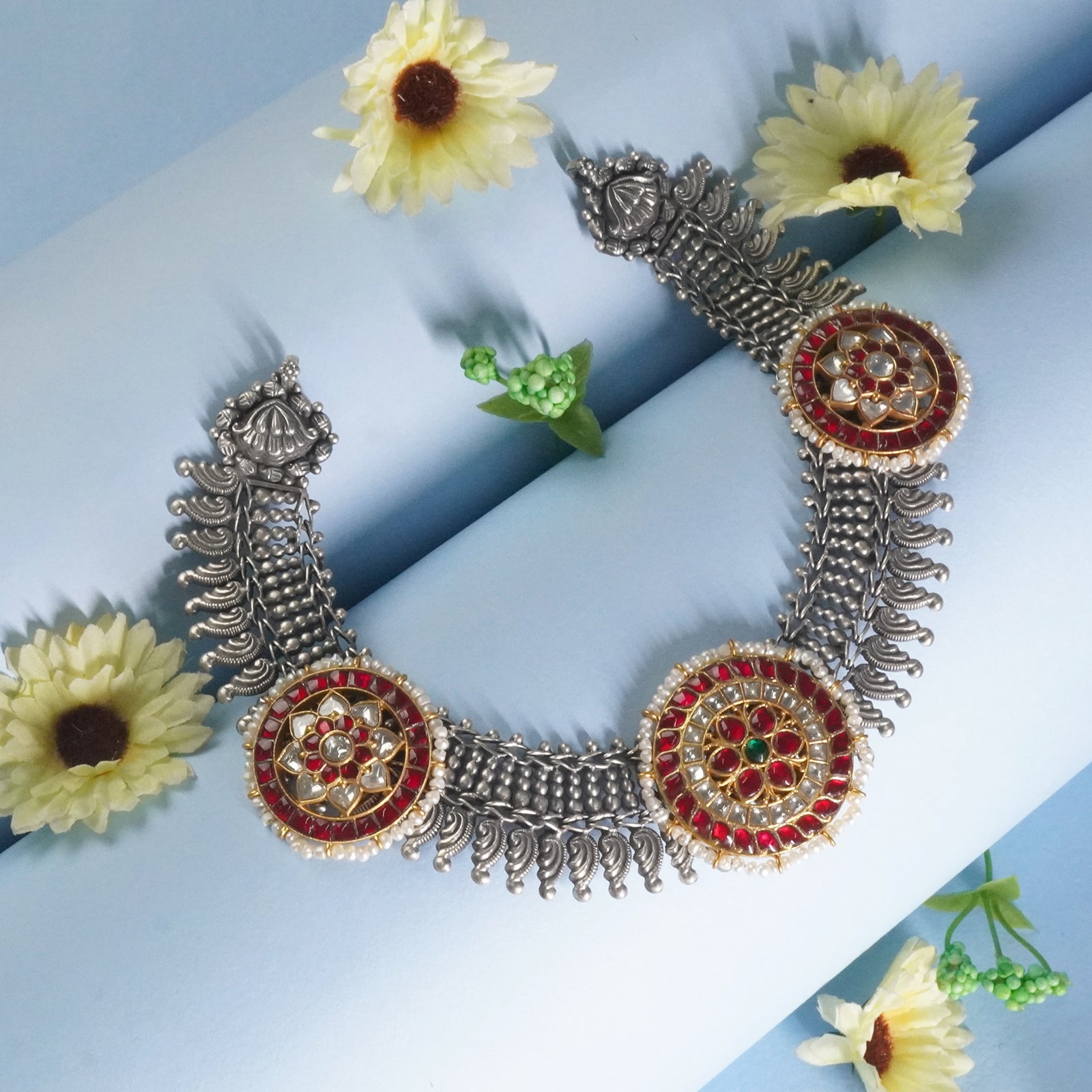 dual tone silver and red necklace on a light blue background with yellow flowers